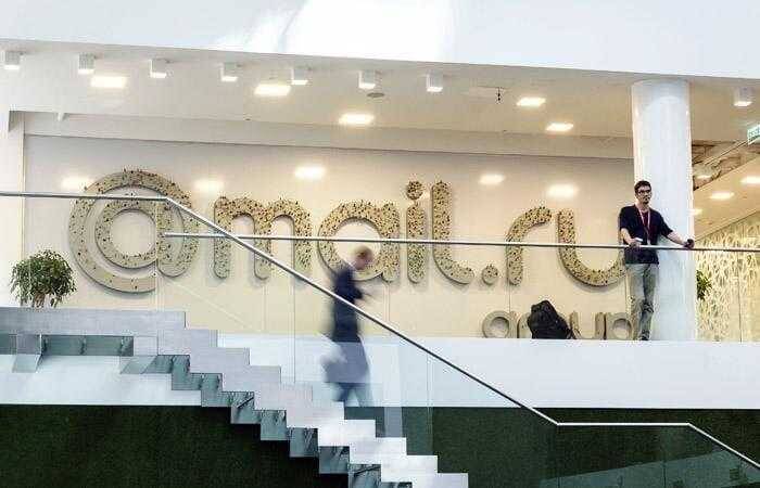 Люди на фоне стены с надписью Mailru в офисе
