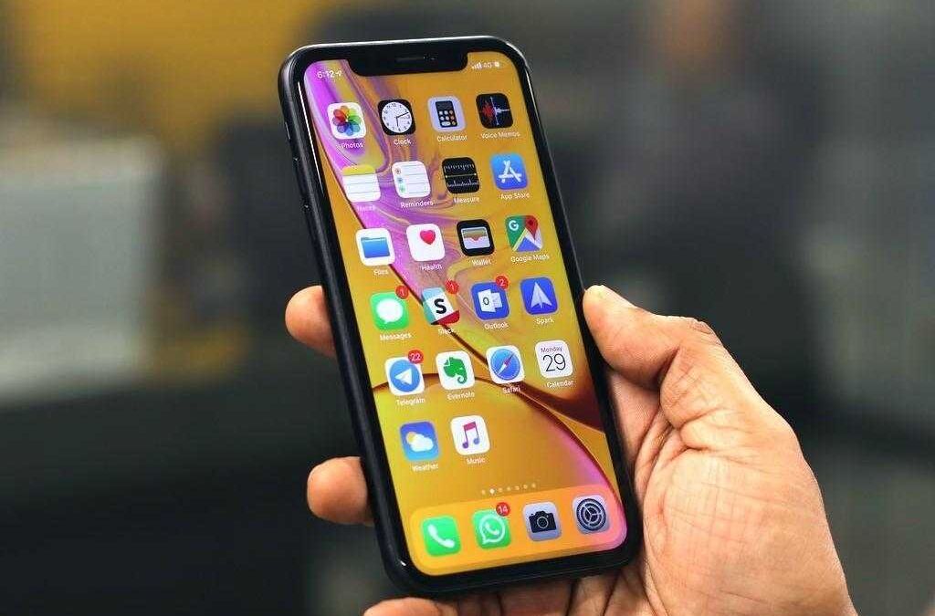 Рука держит iPhone с дисплеем, показывающим иконки приложений