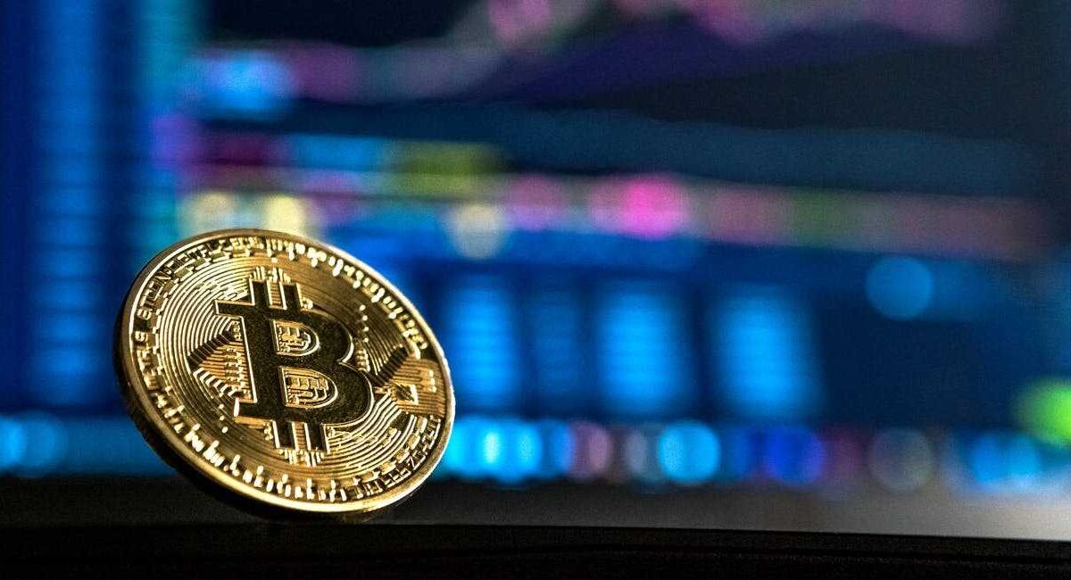 Медная биткоиновая монета на фоне графика торгов криптовалютами