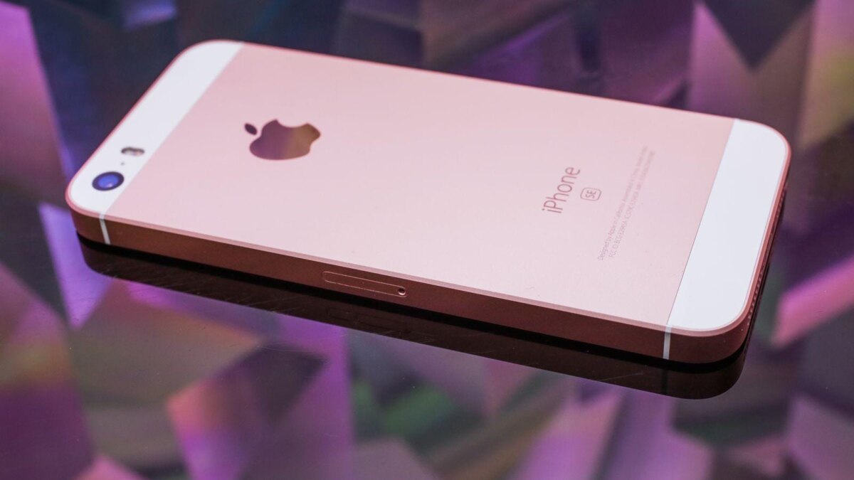 Розовый iPhone SE лежит на стеклянной поверхности