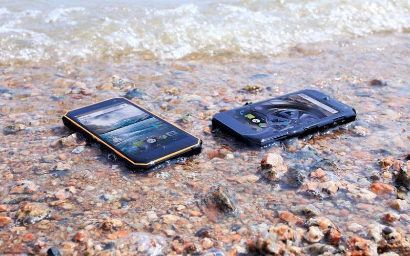 Два защищённых смартфона в воде на каменистом берегу