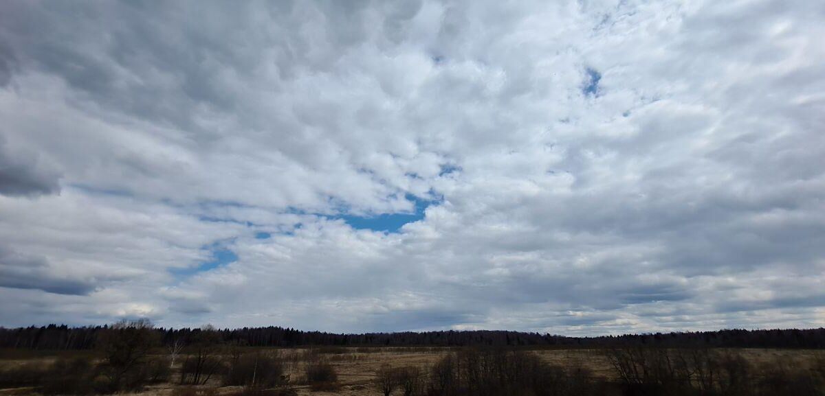 Облака над простором с полем и деревьями на заднем плане