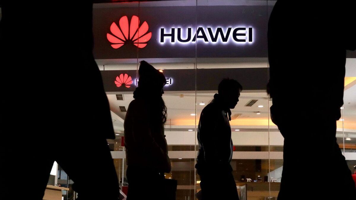 Силуэты людей внутри торгового центра перед логотипом Huawei