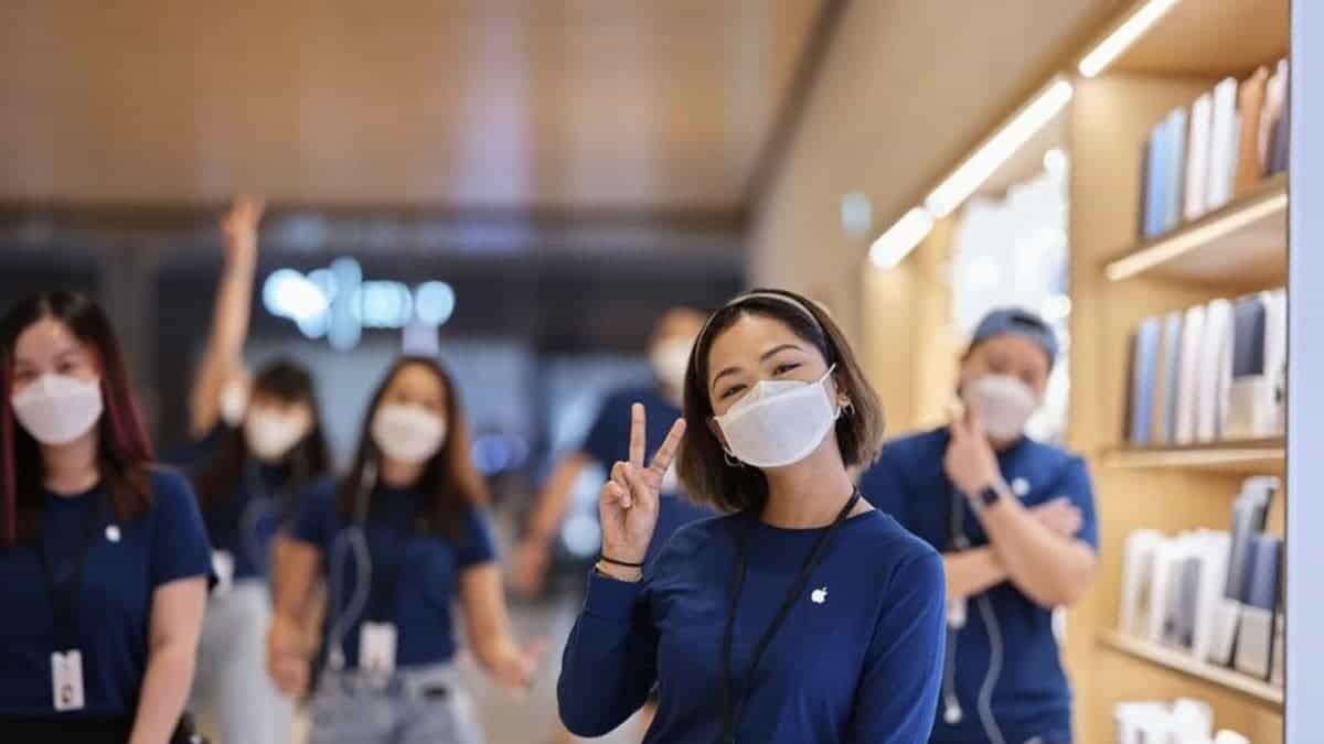 Женщина в маске и фирменной одежде Apple в магазине