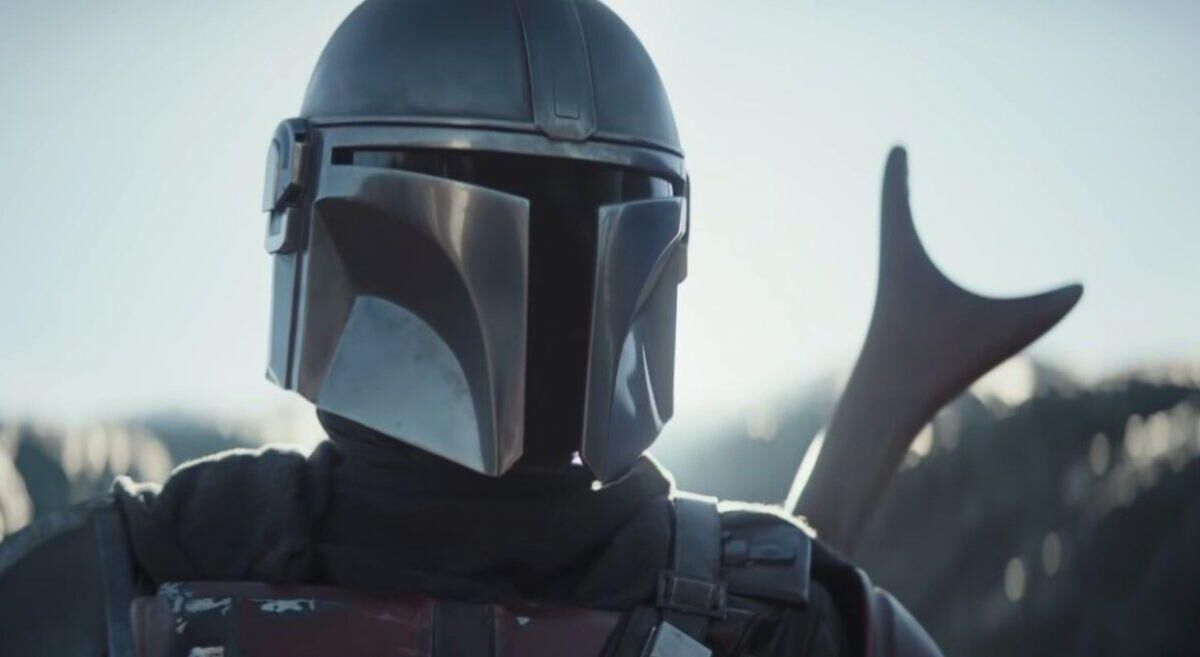 Мандалорец в шлеме показывает жест рукой с отражением солнца