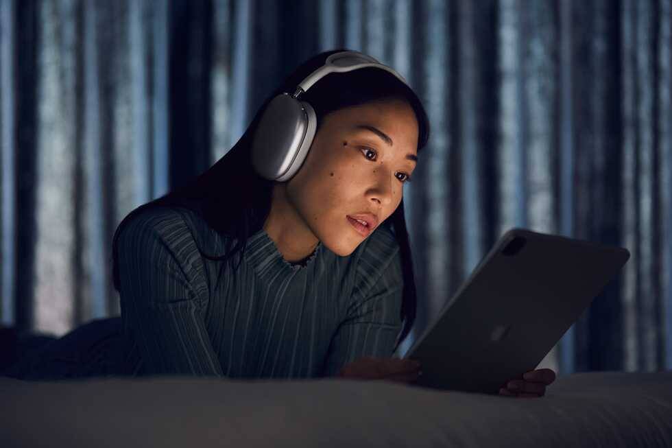 Apple работает над более дешевой версией AirPods Max 3 Девушка в наушниках AirPods Max читает планшет в темной комнате
