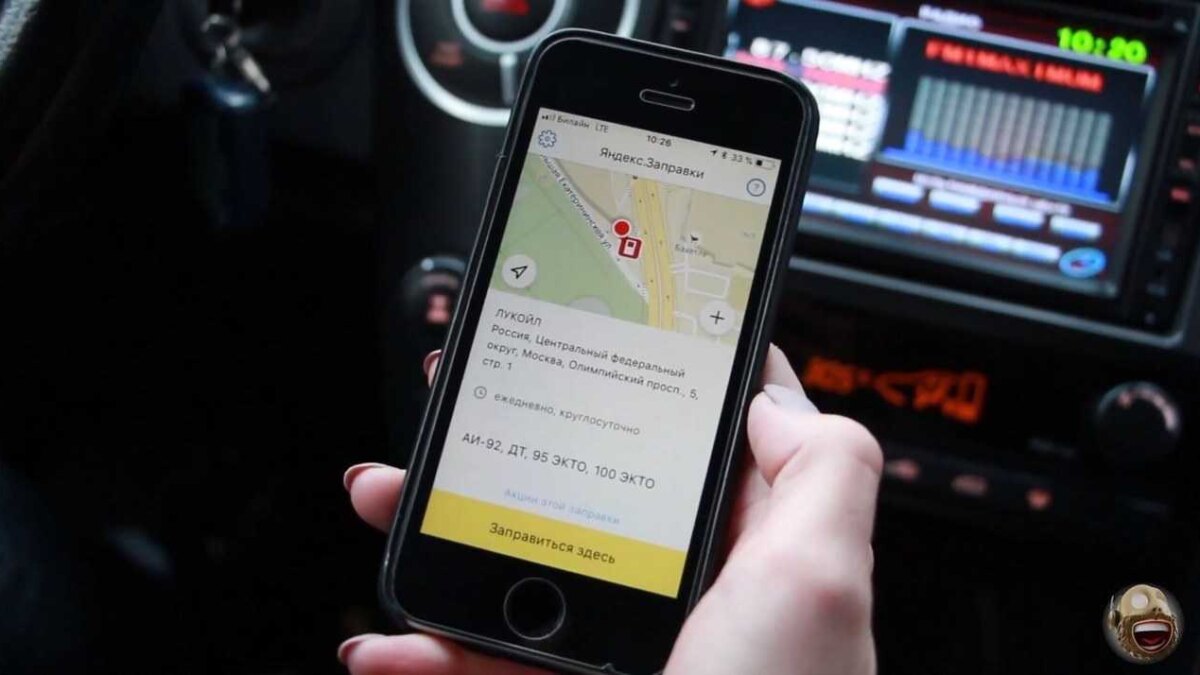 смартфон с приложением Яндекс.Заправки на фоне автомобиля