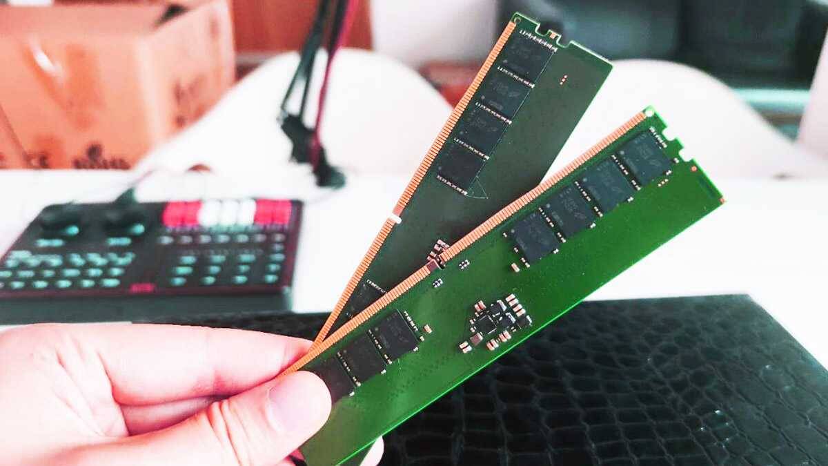 Модули оперативной памяти DDR5 в руке на фоне материнской платы и калькулятора