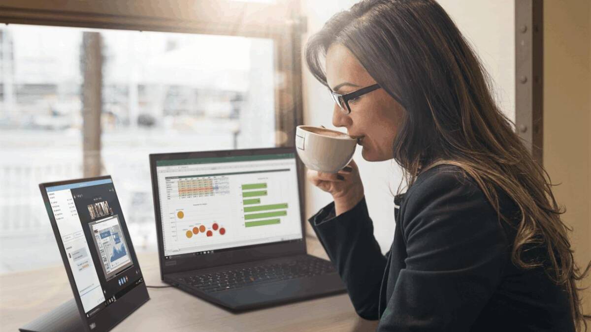 Женщина работает за ноутбуком и монитором Lenovo ThinkVision в современном офисе