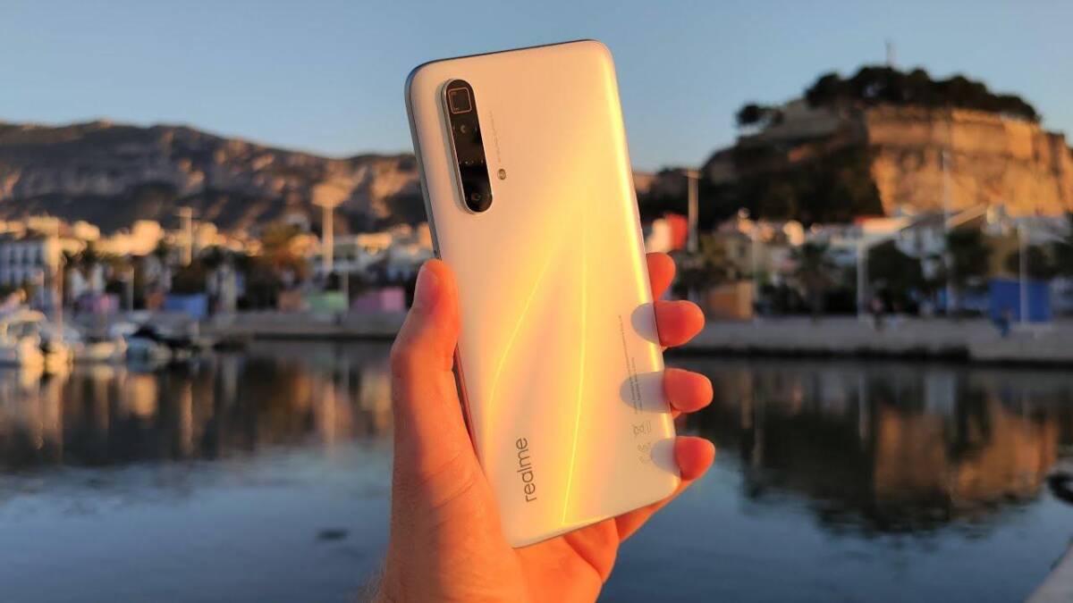 Белый смартфон Realme с тройной камерой на задней панели у воды