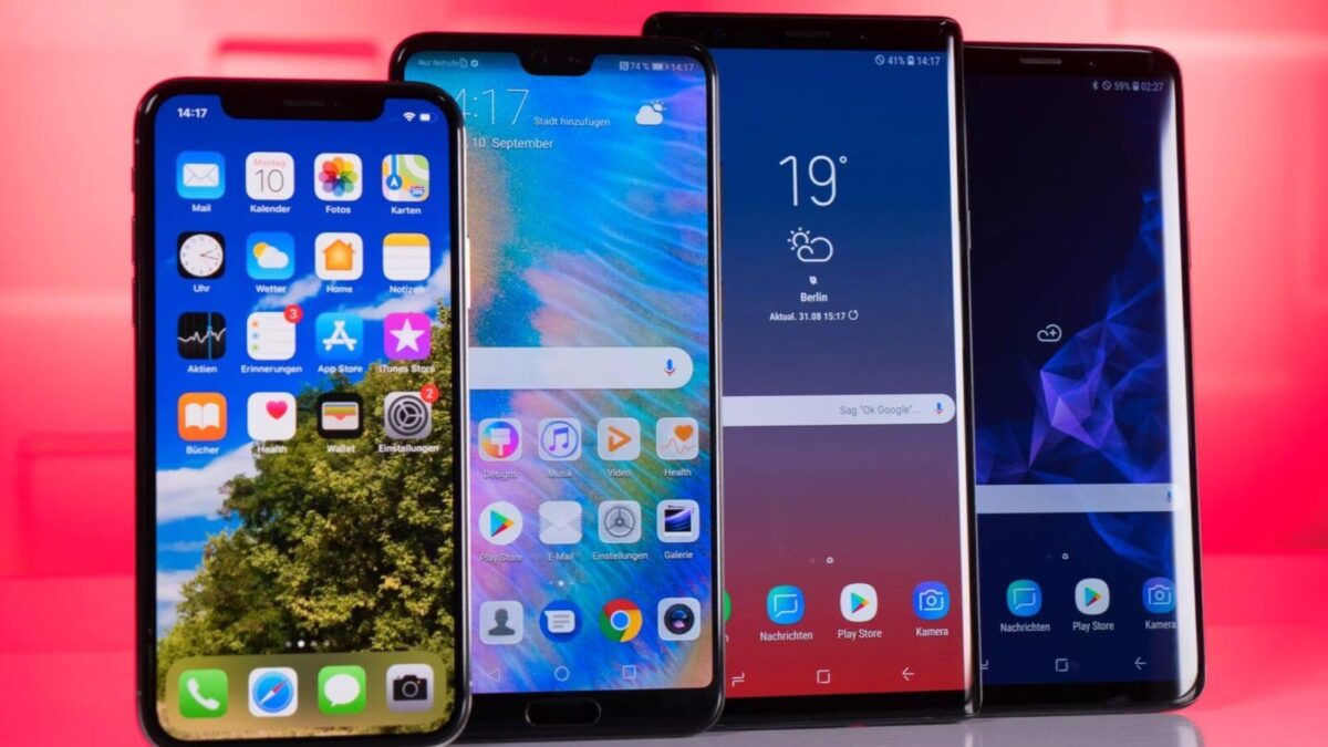 Пять Android-смартфонов Samsung на столе, разные модели с интерфейсами на фоне красной стены