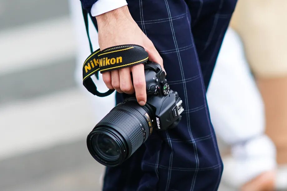 Фотограф держит зеркальный Nikon с крупным зум-объективом в руке, кадр о выходе бренда с рынка