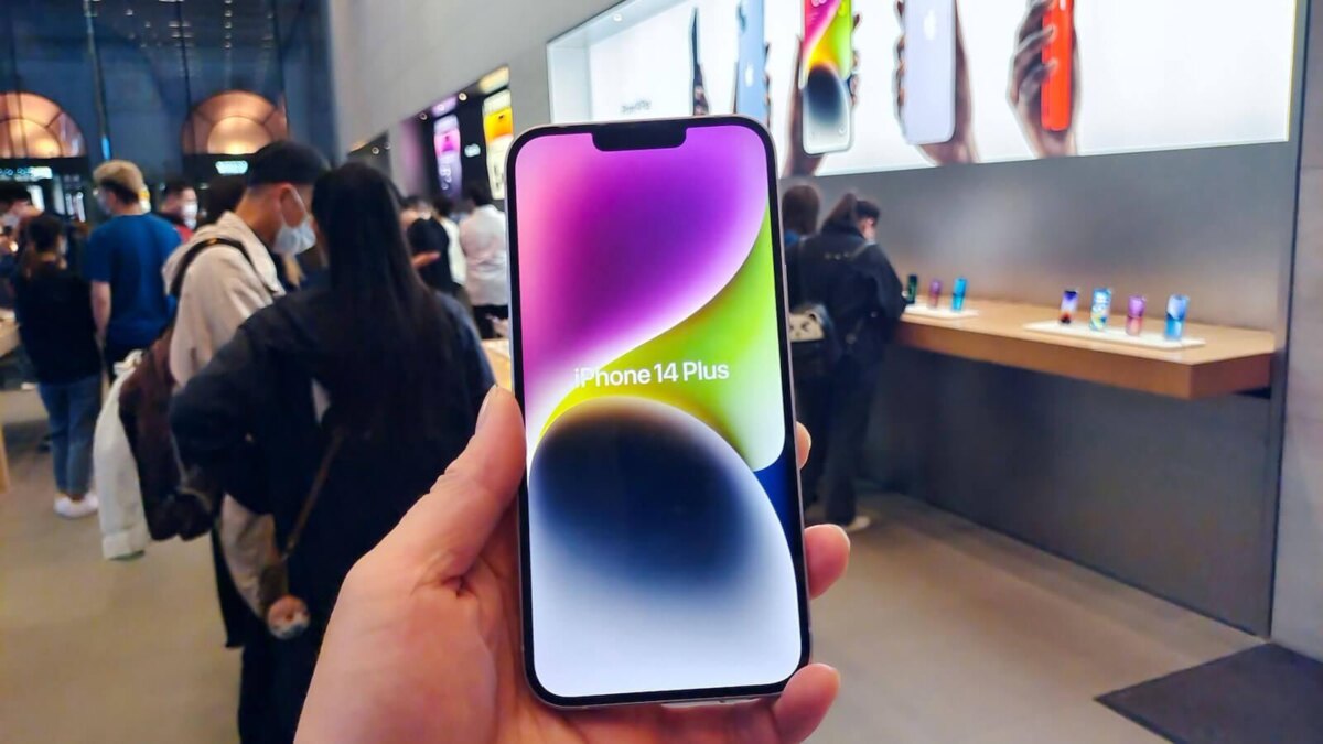 Рука держит iPhone 14 Plus в магазине с людьми на заднем плане