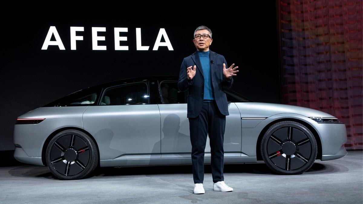 Человек на сцене с электромобилем Afeela на фоне логотипа