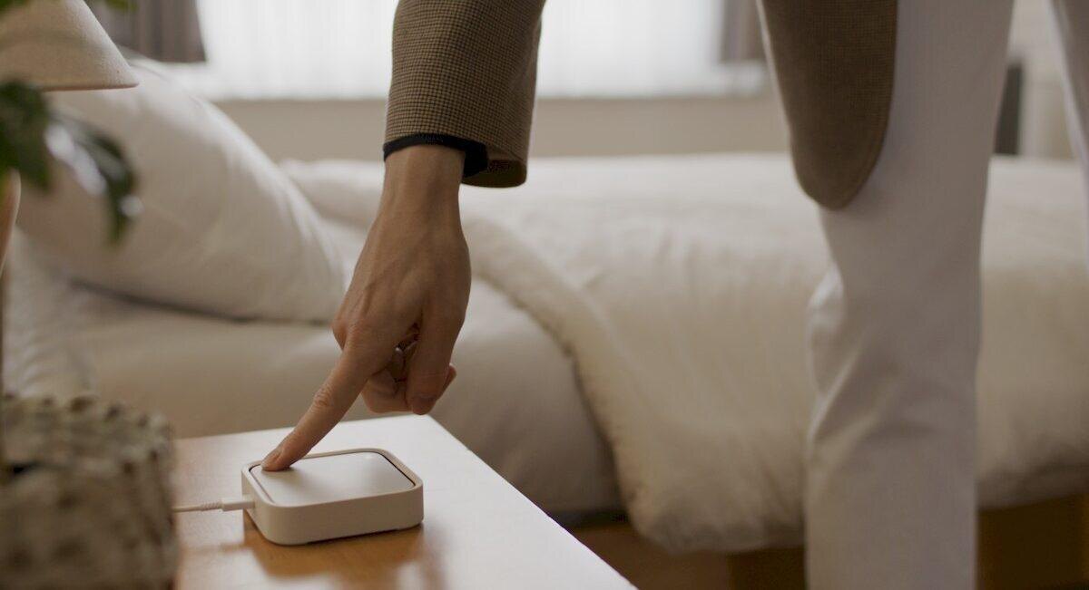 Палец касается Samsung SmartThings Station на прикроватной тумбочке, управление умным домом