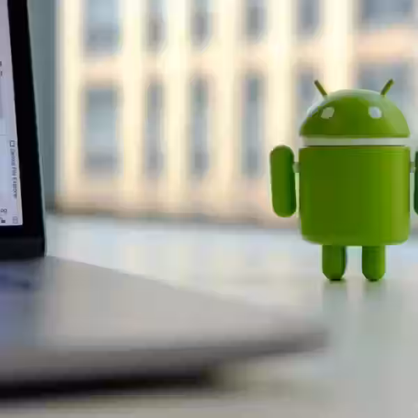 Зеленая фигурка Android 15 у компьютера на столе