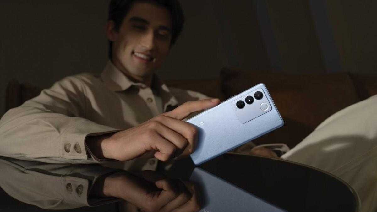 Мужчина держит смартфон Vivo V27 в руке в темной обстановке