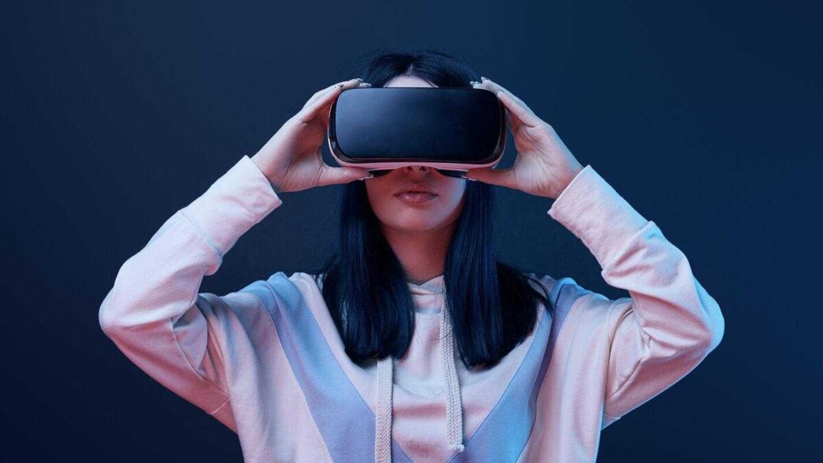 Девушка в VR-гарнитуре на темном фоне в тренировочной толстовке использует VR-шлем