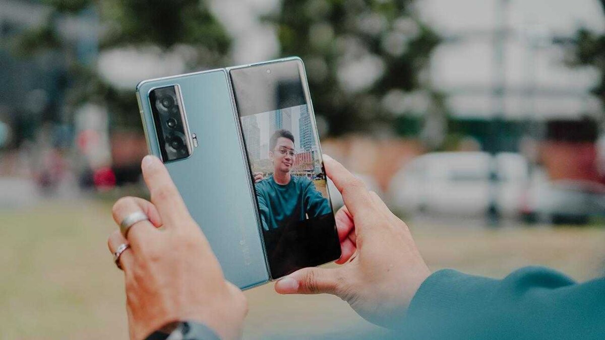 Человек фотографирует складной смартфон Honor Magic V2 на улице