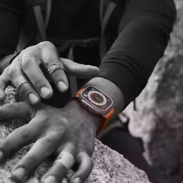 Человек проверяет умные часы Apple Watch Ultra на руке у скального выступа