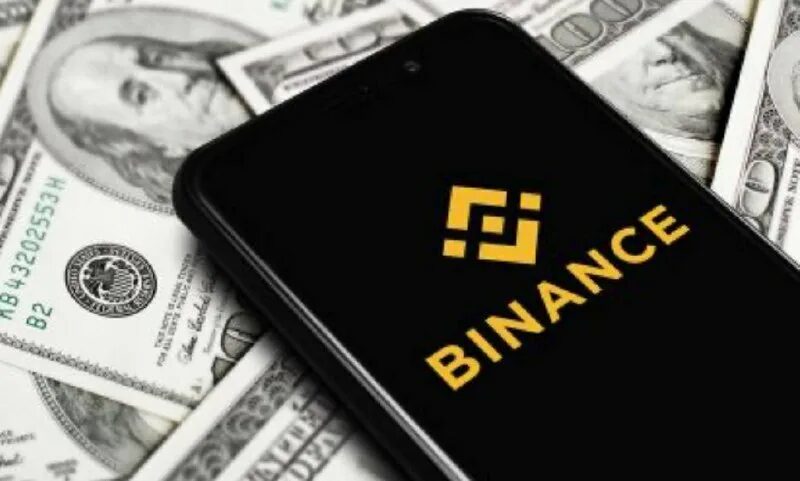 Смартфон с логотипом Binance на экране и наличные деньги