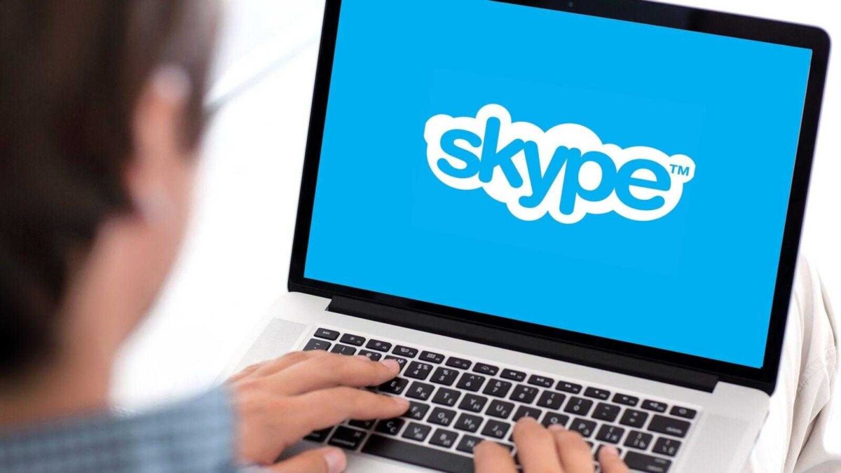 Пользователь печатает на ноутбуке с логотипом Skype, обновленный интерфейс мессенджера на экране
