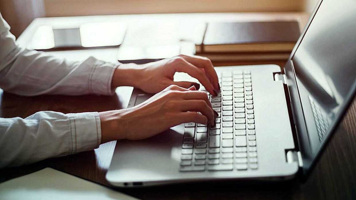 Пользователь печатает на клавиатуре ноутбука с открытым экраном