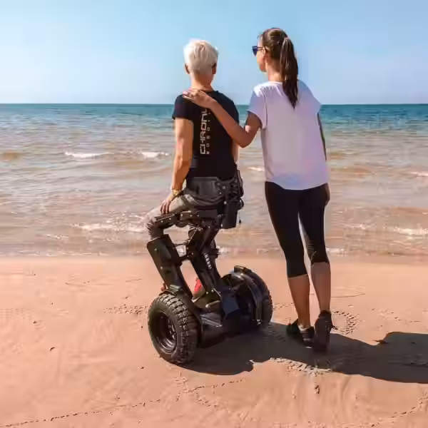 Две женщины на пляже, одна в инвалидной коляске с электроприводом Kim-e
