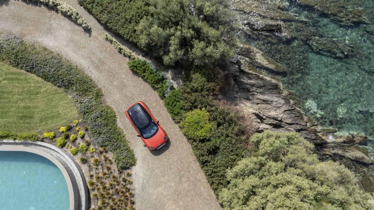 Вид сверху на электромобиль MINI Aceman на дорожке у здания с бассейном и зеленью