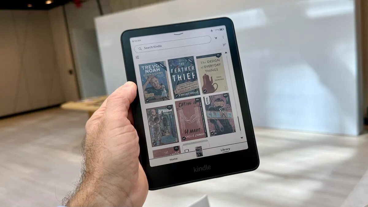 Электронная книга Kindle Colorsoft в руке человека, интерфейс с книжными обложками