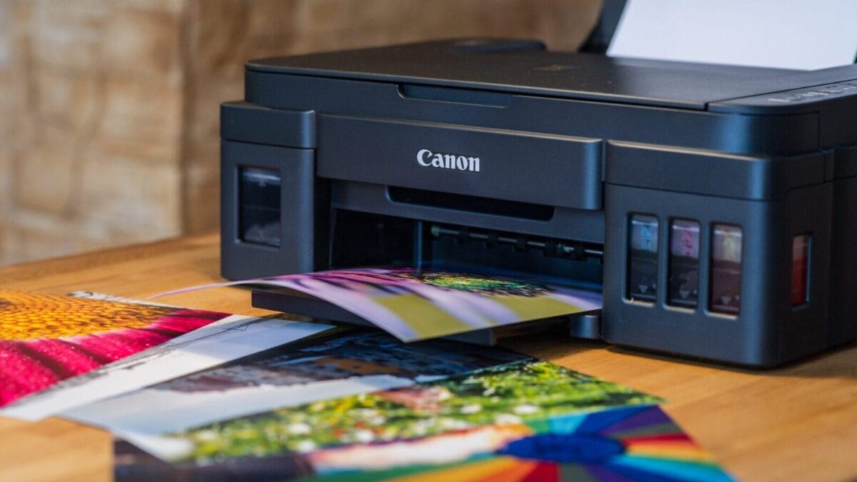 Черный цветной лазерный принтер Canon на деревянном столе печатает яркую цветную фотографию