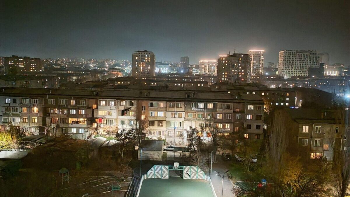 Вид с балкона на зажжённые окна многоэтажных домов и детскую площадку