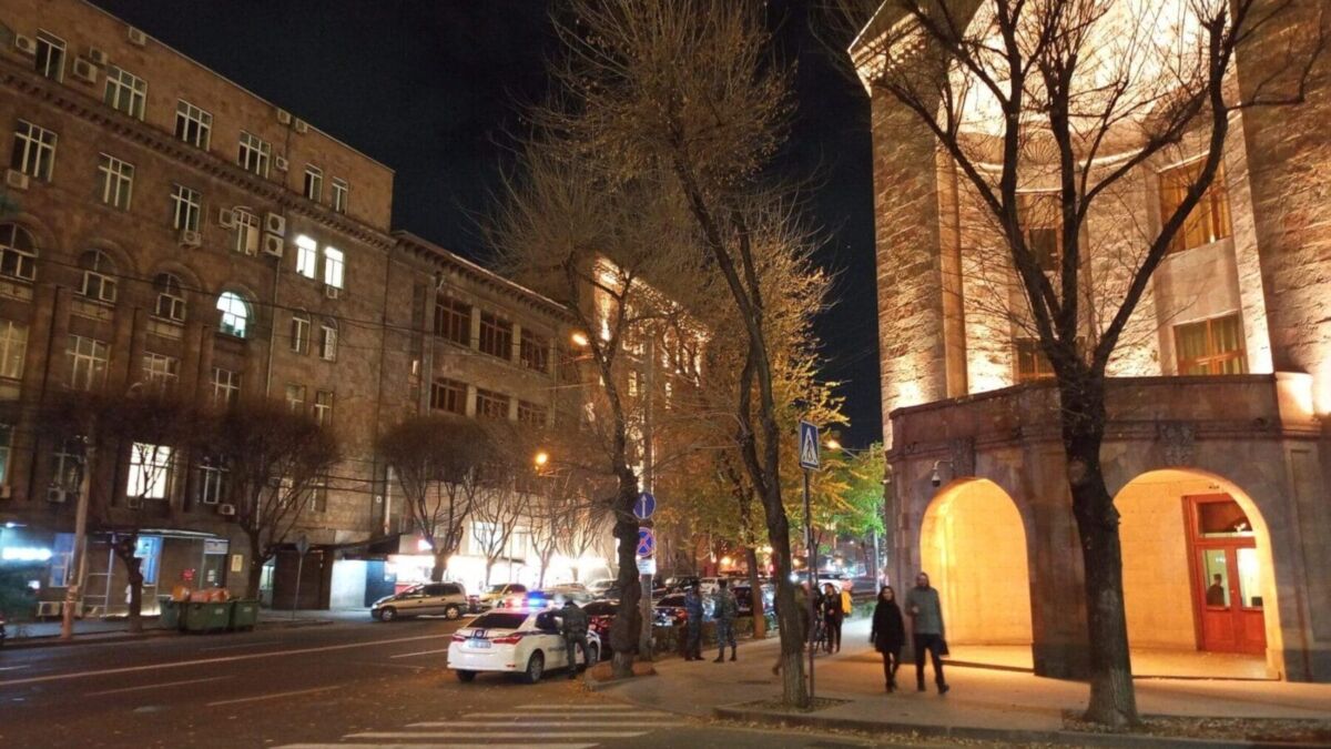 Ночной городской пейзаж с освещенными зданиями и людьми на улице на фоне освещенного здания с арками