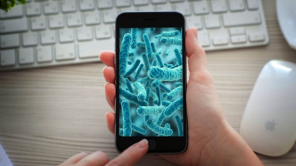 iPhone с бактериальными изображениями на экране в руках пользователя, намек на вирус SparkCat