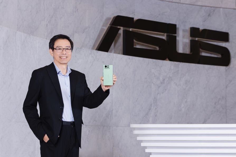 Человек в деловом костюме держит смартфон Asus Zenfone 12 Ultra у стены с логотипом компании