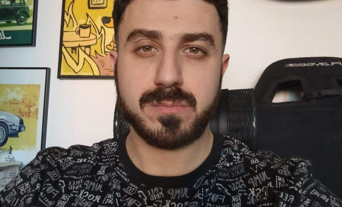 Мужчина в футболке с текстом на фоне настенной галереи и гитары