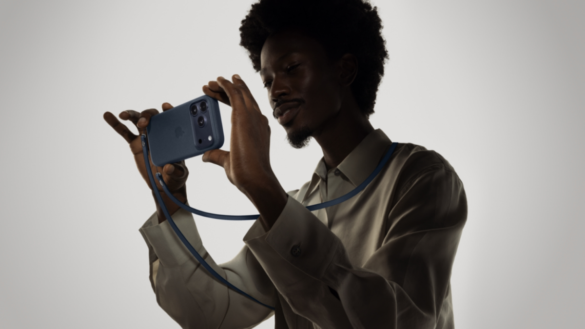 Человек держит синий iPhone и проводные наушники на презентации Apple