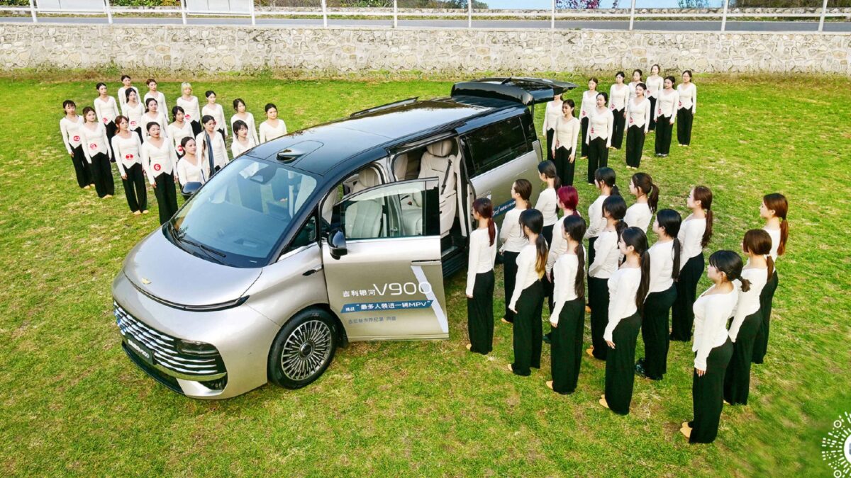 42 человека в салоне Geely Galaxy V900 на лужайке с рядом припаркованным электромобилем Geely