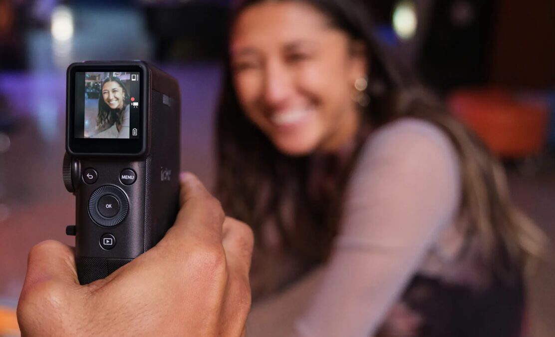 Рука держит камеру Fujifilm instax mini Evo для съемки портрета женщины в кафе