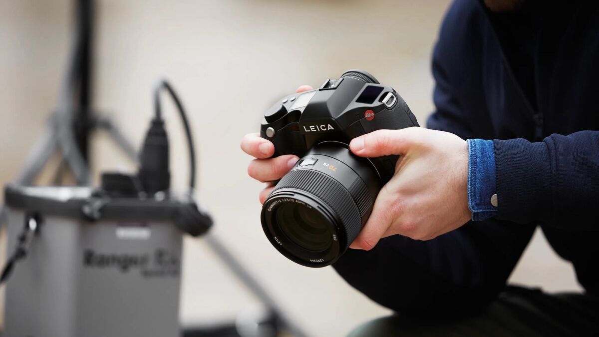 Рука держит среднеформатную камеру Leica с крупным объективом