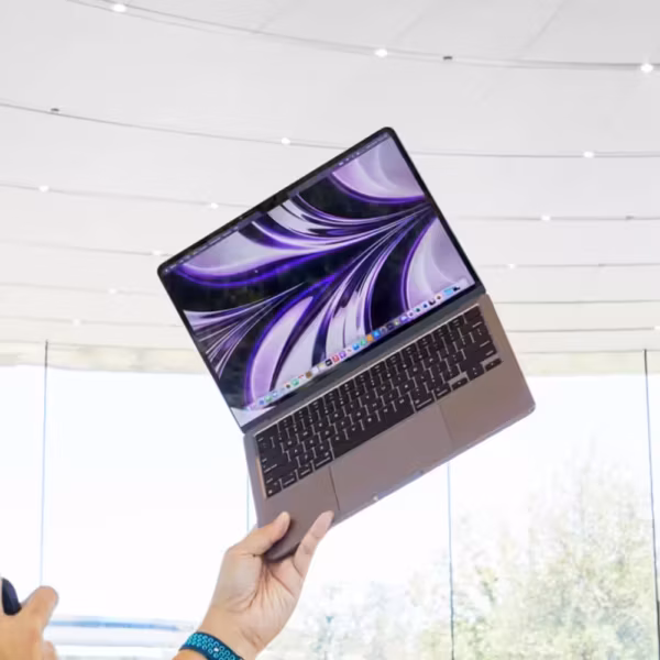 Человек держит MacBook Air Purple с ярким дисплеем на выставке, видна клавиатура и трекпад