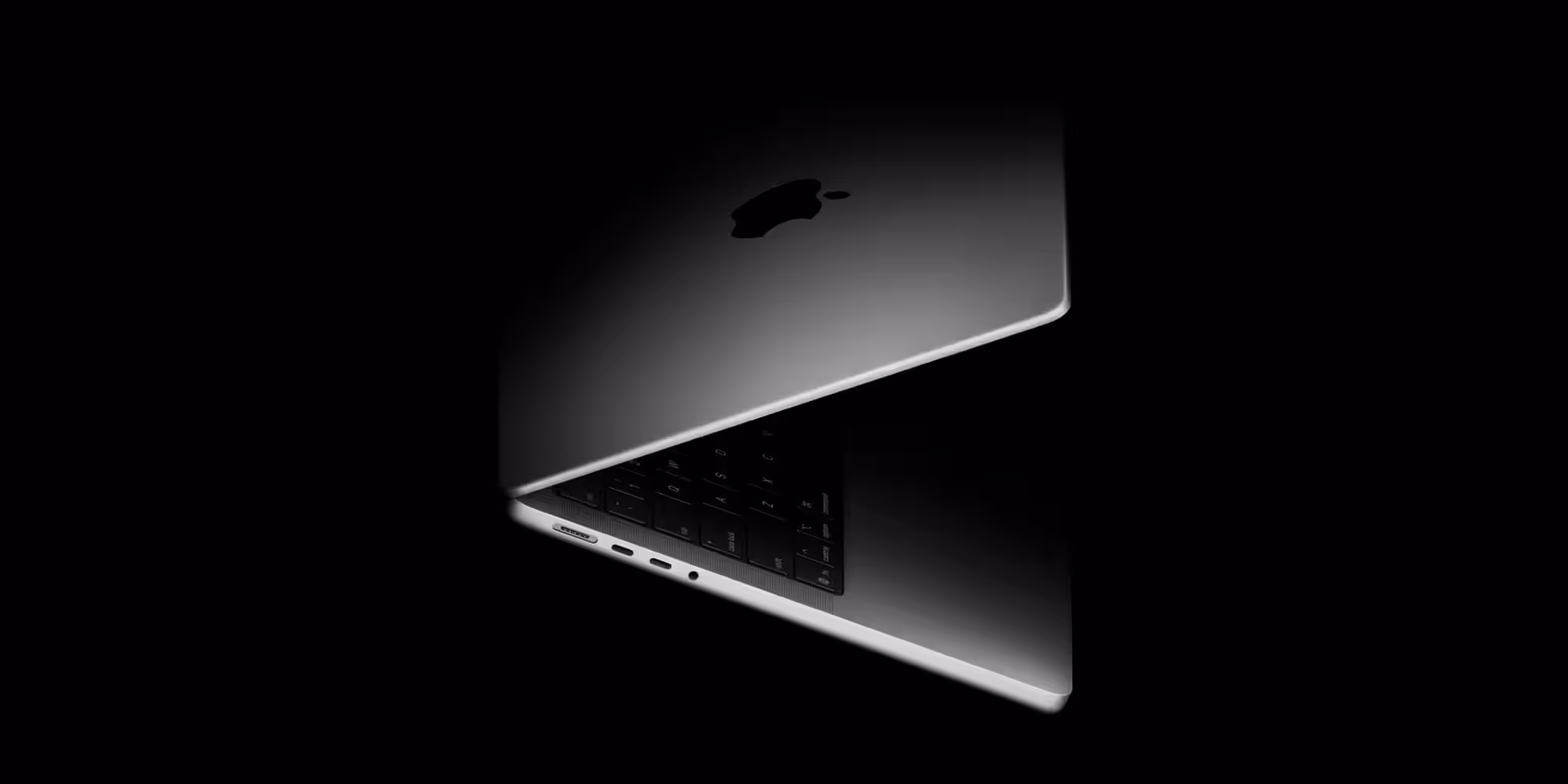 Часть ноутбука MacBook с открытым дисплеем и клавиатурой в тенях