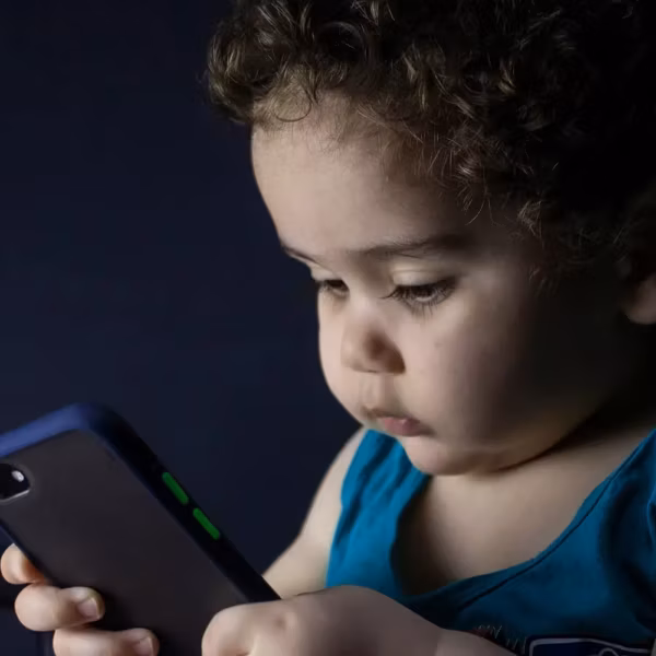 Ребёнок с темными волосами использует iPhone в темной комнате