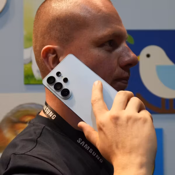 Человек держит белый смартфон Samsung Galaxy S26 возле уха на выставке