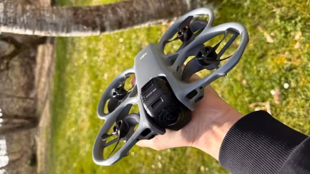 Рука держит квадрокоптер DJI Avata 360 на улице