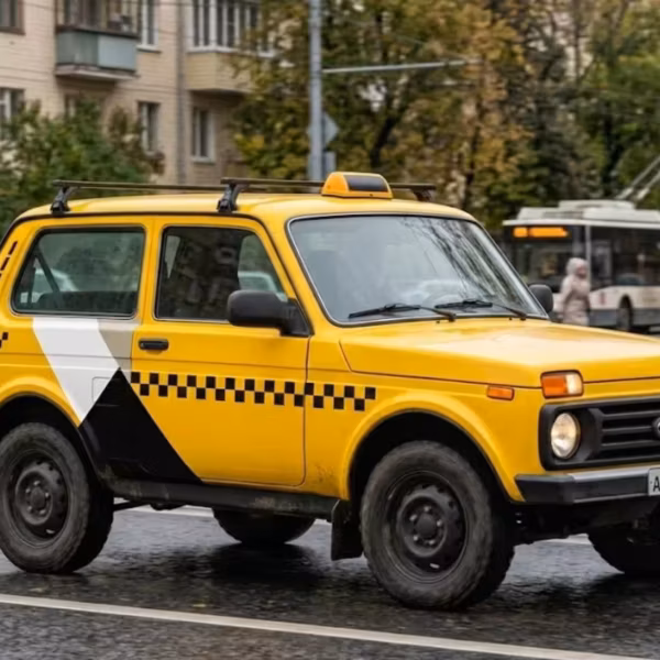 Жёлтая таксомоторная машина на городском шоссе, иллюстрация списка Минпромторга для такси с 1 марта 2026