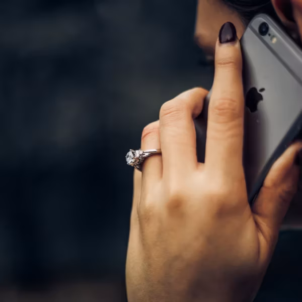 Женщина держит iPhone и показывает кольцо на пальце на фоне предупреждения о мошеннических звонках МТС