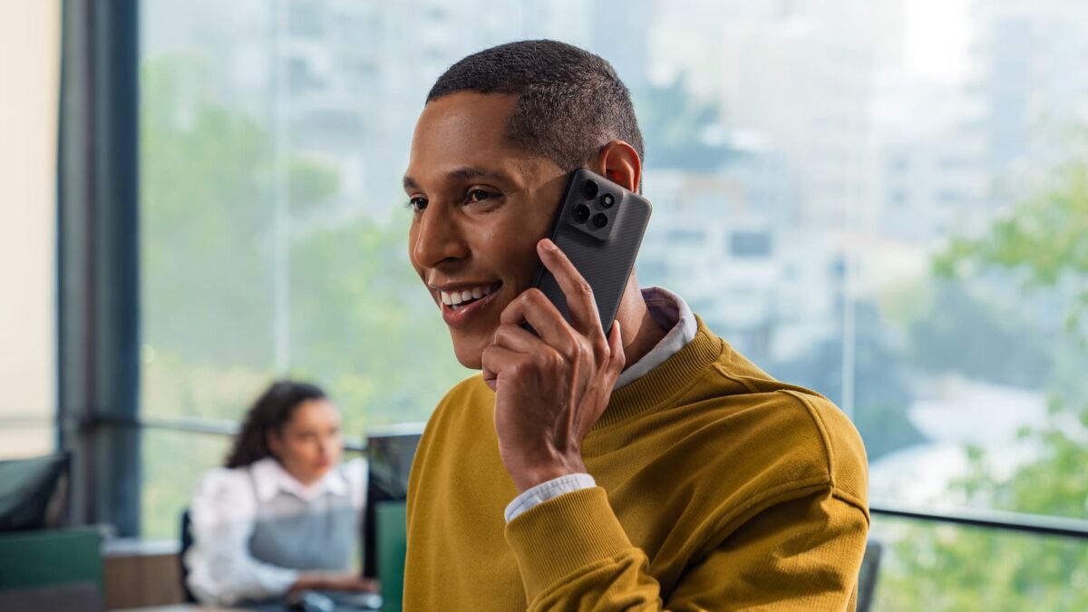 Мужчина в офисе разговаривает по смартфону Motorola с черным корпусом на фоне запуска поддержки GrapheneOS
