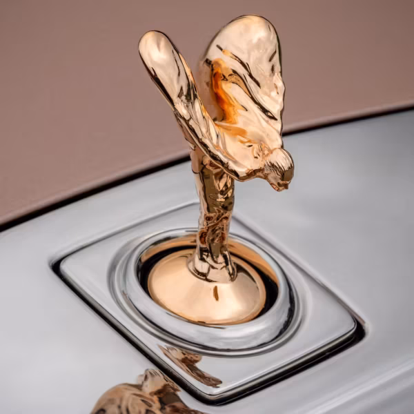 Золотая сувенирная статуэтка Rolls-Royce «Дух экстаза» на фоне логотипа бренда