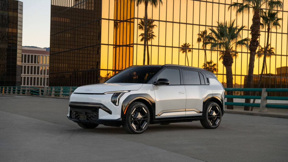 Электромобиль Kia EV3 2027 на дороге у зданий с панелями из стекла и пальмами